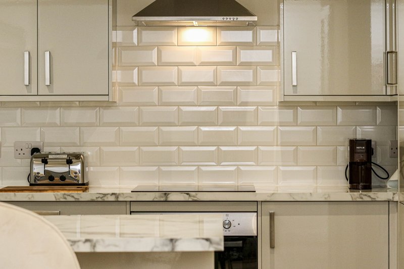 Modern kitchen with cream subway tile backsplash, white cabinets, stainless steel countertop and appliances