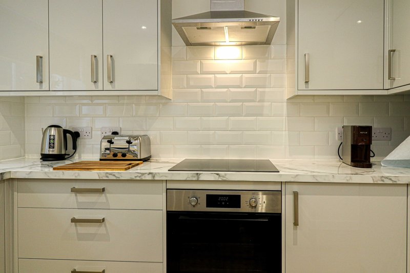 Modern white kitchen with stainless steel oven, kettle, coffee machine and subway tile backsplash