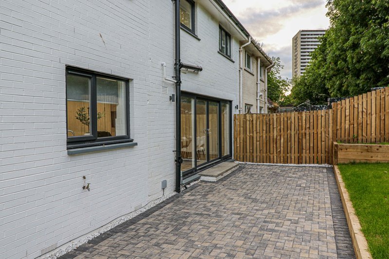 White brick house exterior with patio, wooden fence, and manicured garden area