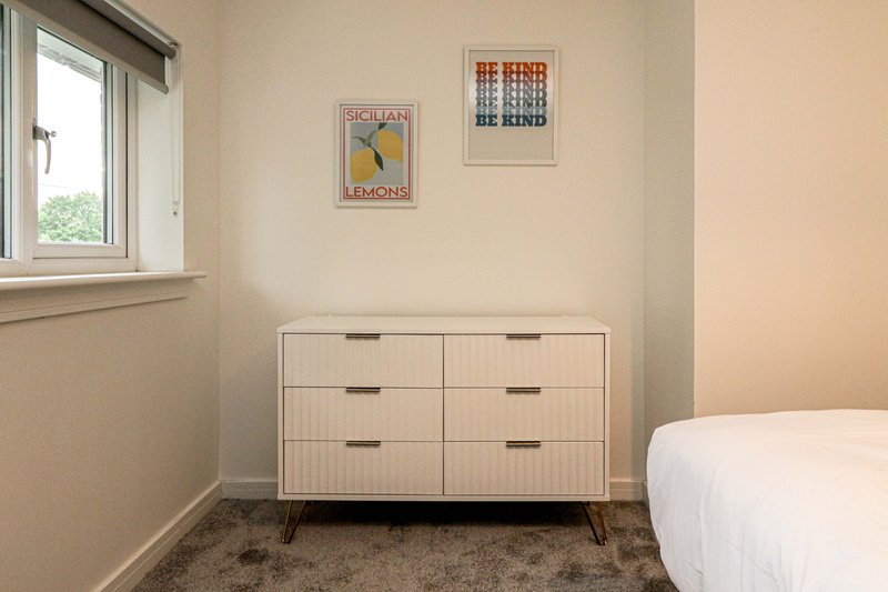 Bright bedroom with white dresser, framed posters, window with natural light and single bed