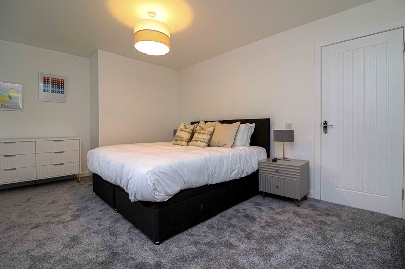 Bedroom with queen bed, black frame, white bedding, gold cushions, nightstand and ceiling light