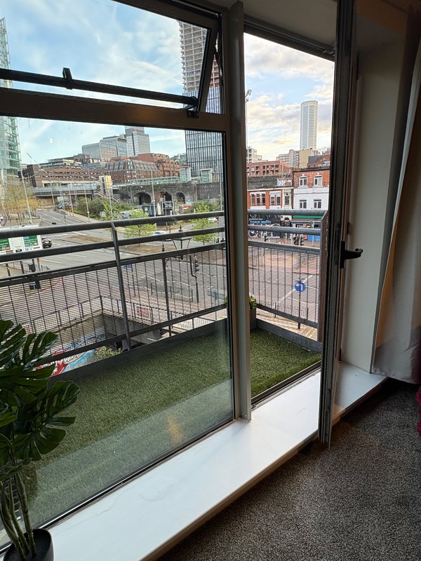 Balcony with glass doors overlooking urban cityscape, green artificial turf, and potted plant