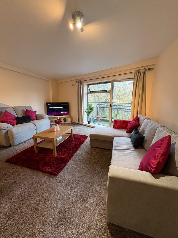 Spacious living room with two cream sofas, red rug, wooden table and large windows