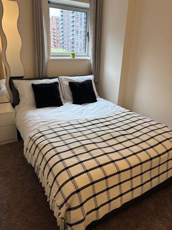 Modern bedroom with double bed, striped bedding, black cushions, window with city view