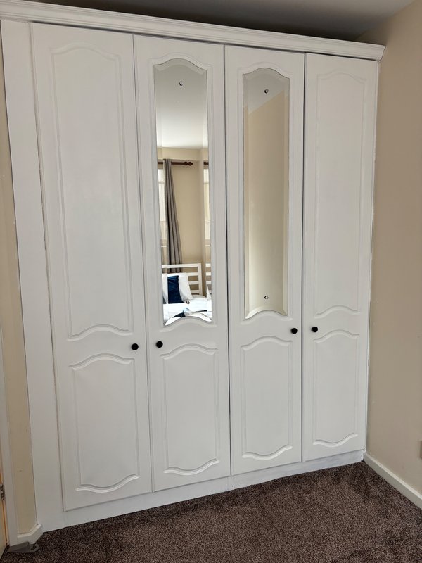 White four-door wardrobe with mirrored panels in bedroom with brown carpet