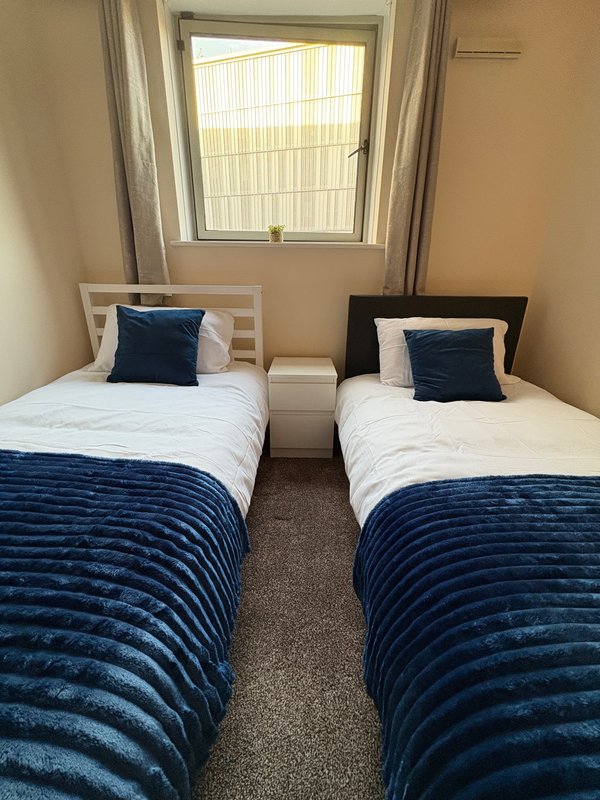 Twin bedroom with two single beds, blue quilts, navy cushions, and window with vertical blinds