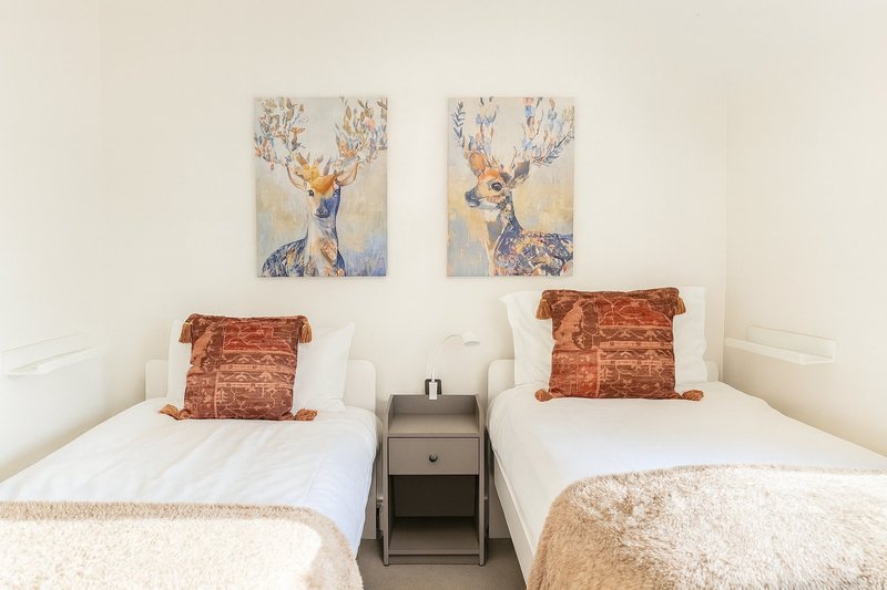 Twin bedroom with two single beds, bedside table, deer artwork and rust-colored cushions