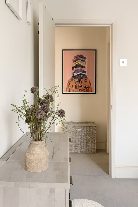 Bright hallway with pale walls, vase of dried flowers on floor, framed artwork on wall