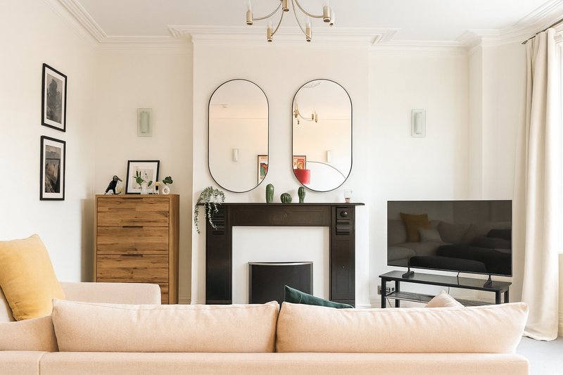 Bright living room with cream sofa, fireplace, twin oval mirrors and television