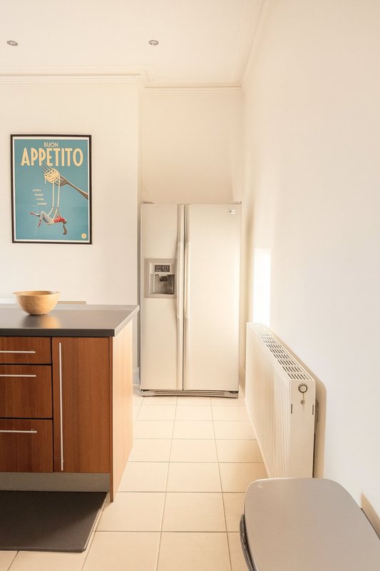 Modern kitchen with wooden cabinetry, stainless steel refrigerator, and vintage appetito wall poster
