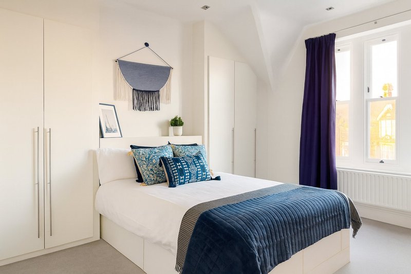 Bright modern bedroom with double bed, blue bedding, wall tapestry, and large window with curtains