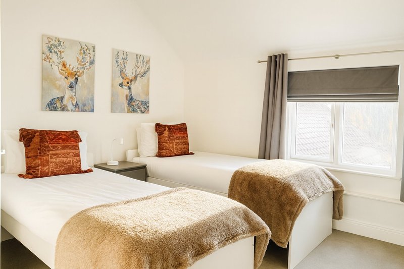 Twin bedroom with two single beds, decorative deer artwork, orange cushions and warm throws