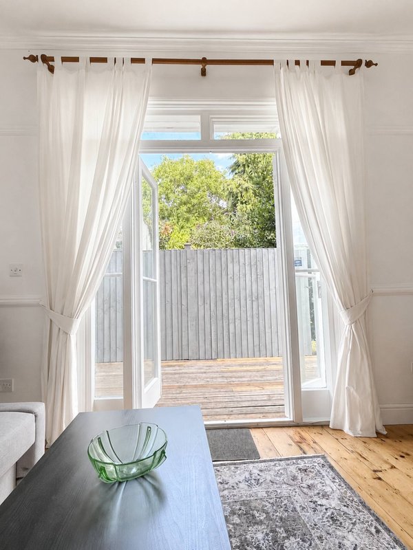 Bright bedroom with French doors opening to balcony, white curtains and wooden flooring