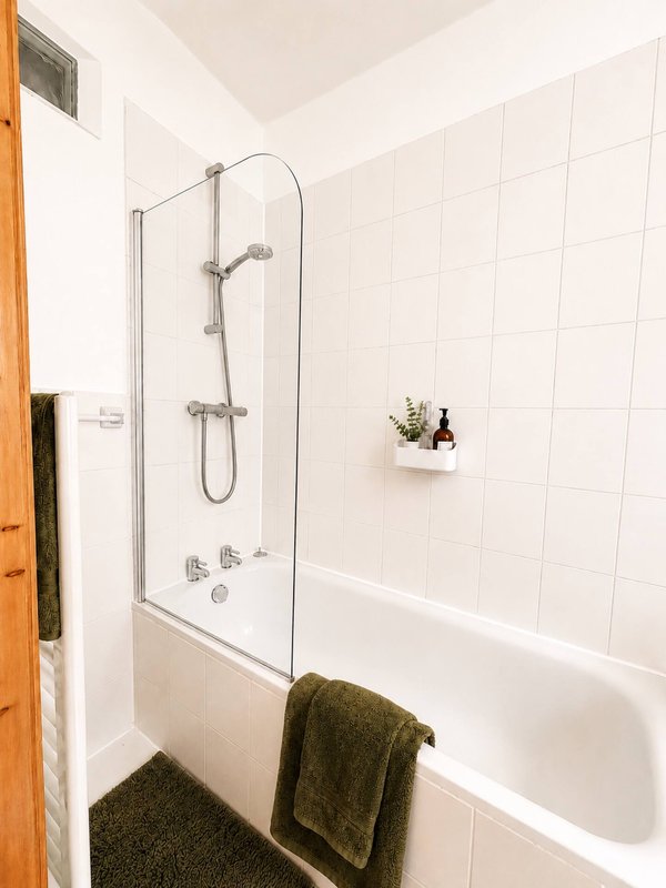 Modern bathroom with white subway tile, glass shower enclosure, bathtub and dark towels