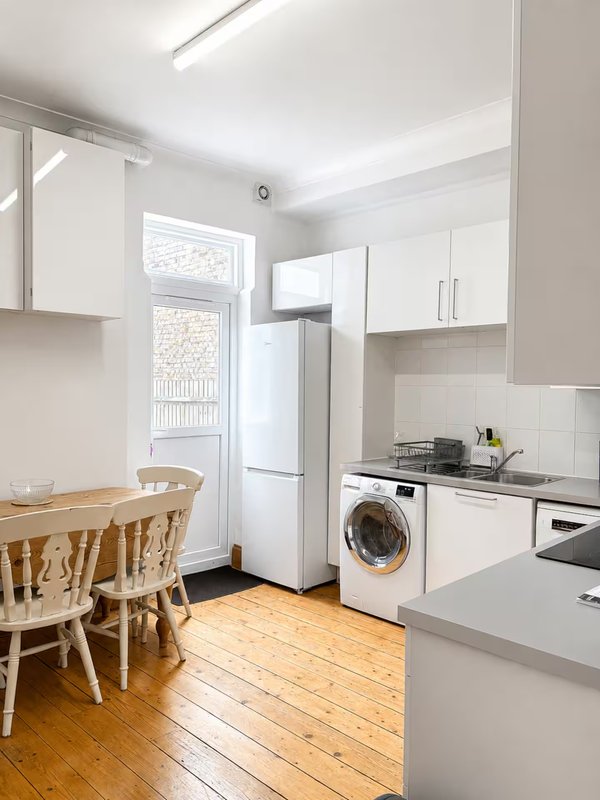 Modern kitchen with white cabinetry, wooden dining table, washing machine and refrigerator