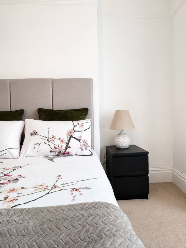 Modern bedroom with upholstered headboard, floral bedding, black nightstand and table lamp