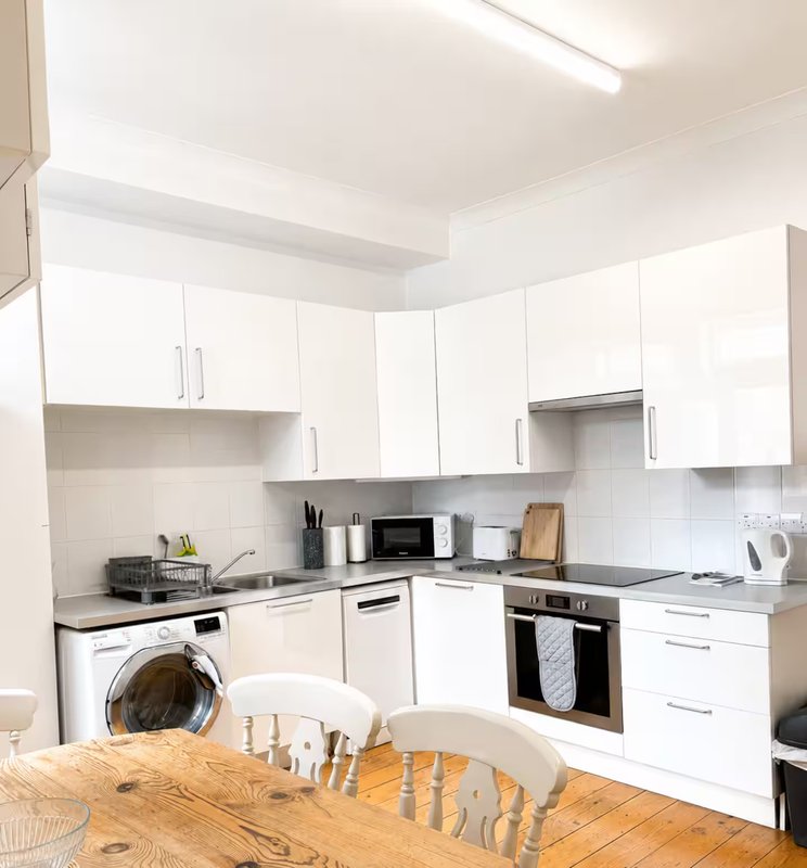 Modern white kitchen with integrated appliances, wooden dining table in foreground