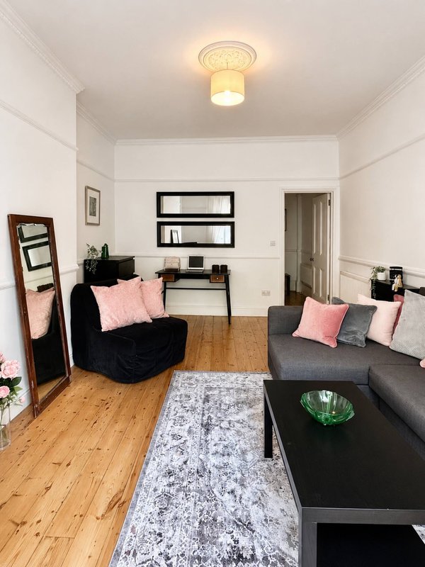 Modern living room with black sofa, pink cushions, wooden flooring and wall shelving