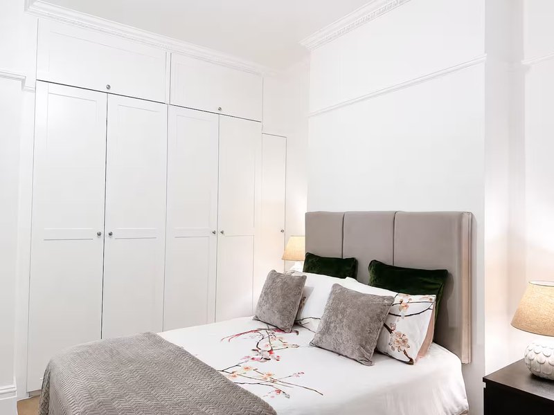 Modern bedroom with double bed, grey upholstered headboard, white built-in wardrobes and bedside lamps