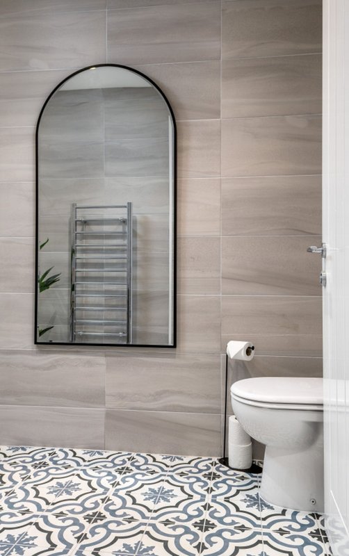 Bathroom with arched mirror, heated towel rail, toilet, and patterned tile floor