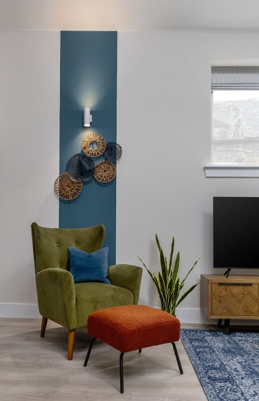 Living room with green armchair, orange ottoman, wall-mounted decorative baskets and pendant light