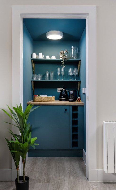 Built-in blue shelving unit with glassware, decorative items, and potted plant in foreground