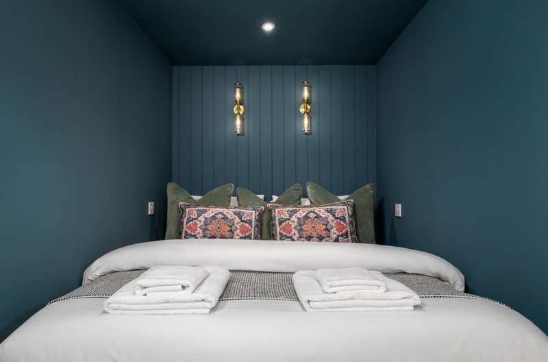 Modern bedroom with teal walls, double bed, decorative pillows, and pendant lighting