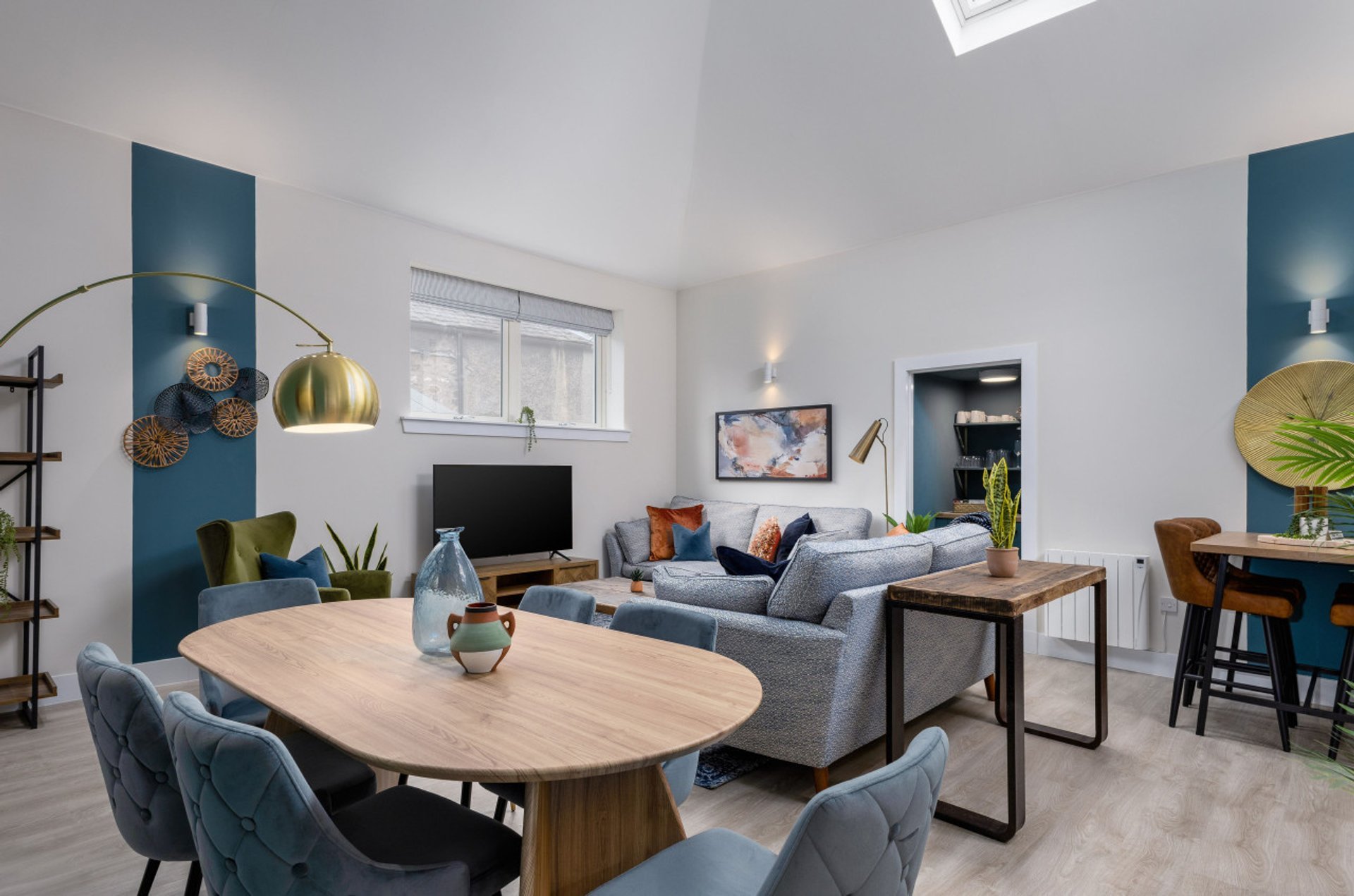 Open-plan living and dining area with wooden table, grey sofa, blue accent walls and modern lighting