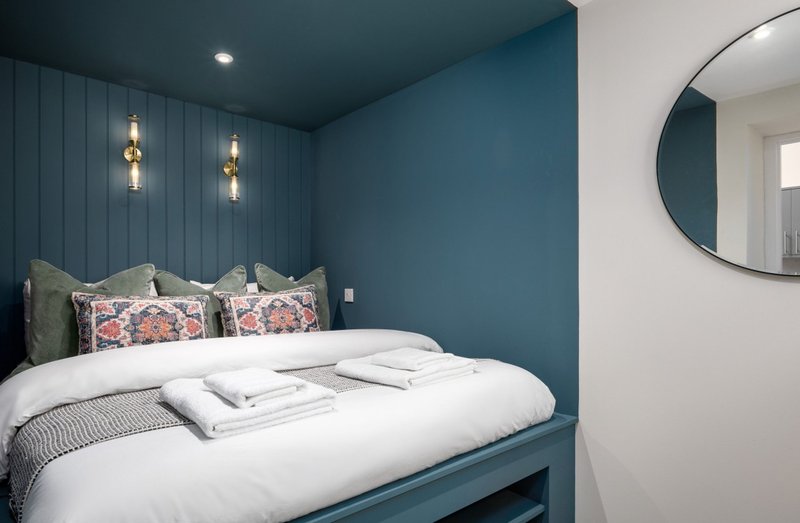 Modern bedroom with teal walls, double bed, decorative pillows and pendant lights