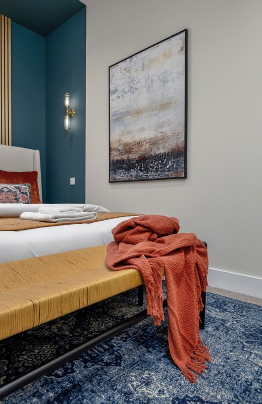 Modern bedroom with white bed, rust-colored throw, abstract wall art, and teal accent wall