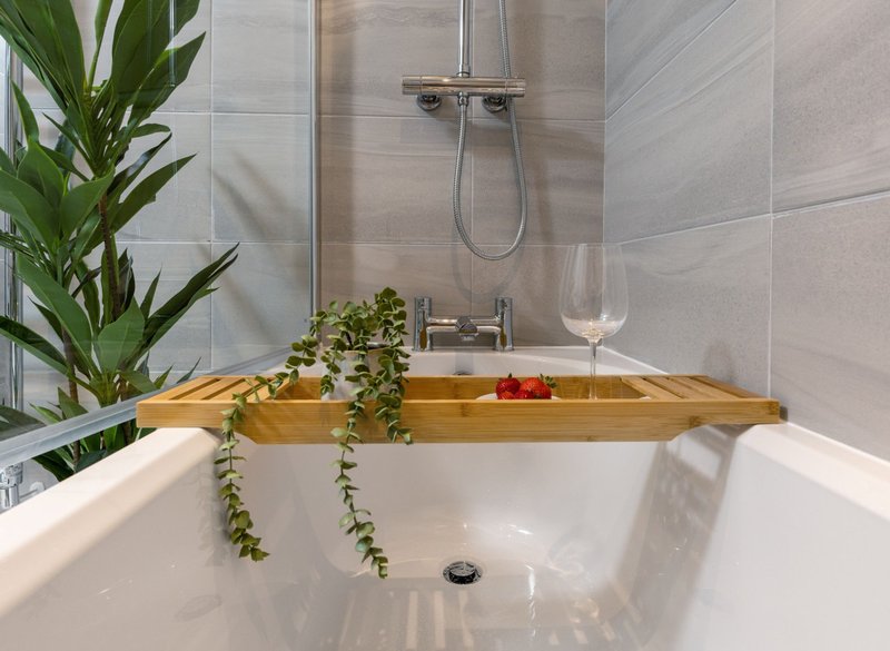 Modern bathroom with white bathtub, wooden bath caddy, potted plants and rainfall showerhead