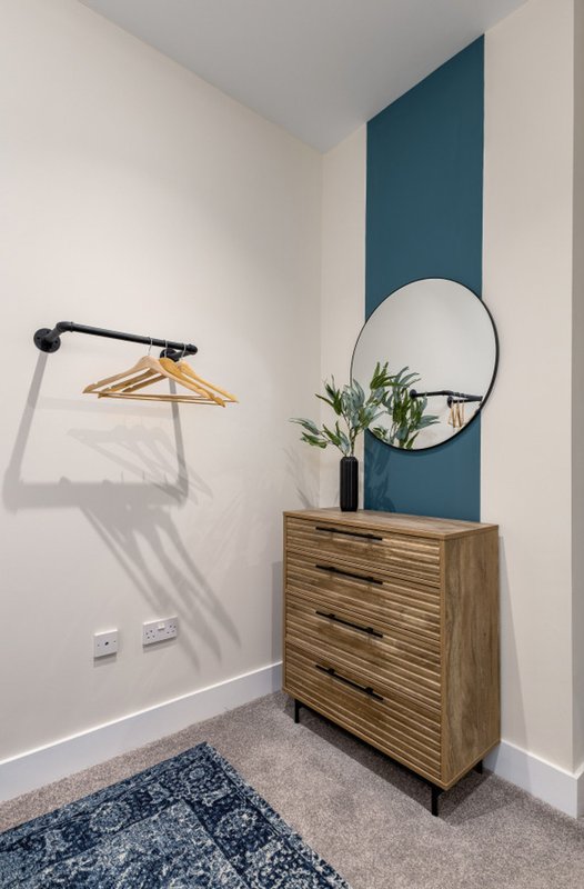 Modern entryway with wooden dresser, round mirror, wall-mounted coat rack and potted plant