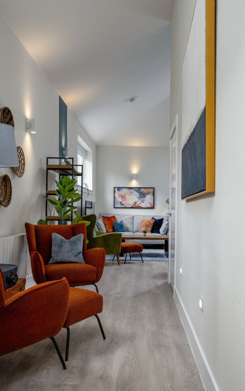 Modern hallway with orange armchair, potted plant, and living room visible through doorway