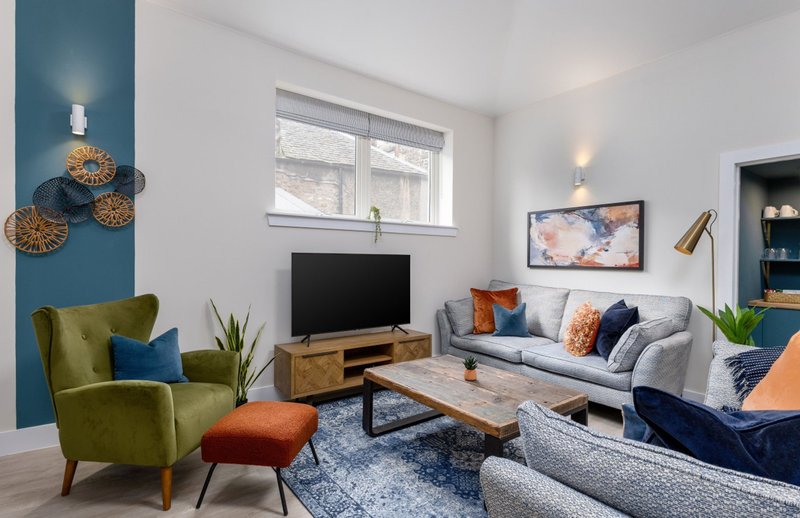 Modern living room with grey sofa, green armchair, wooden TV stand and blue accent wall