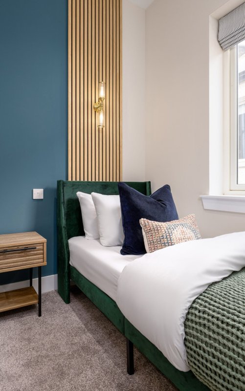 Modern bedroom with green bed frame, white bedding, decorative pillows and wooden accent wall