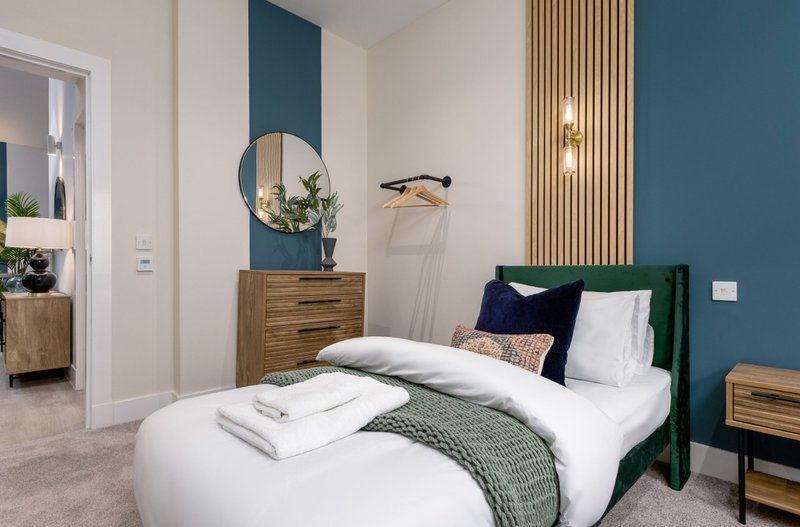 Modern bedroom with green upholstered bed, white bedding, wooden furniture and blue accent wall