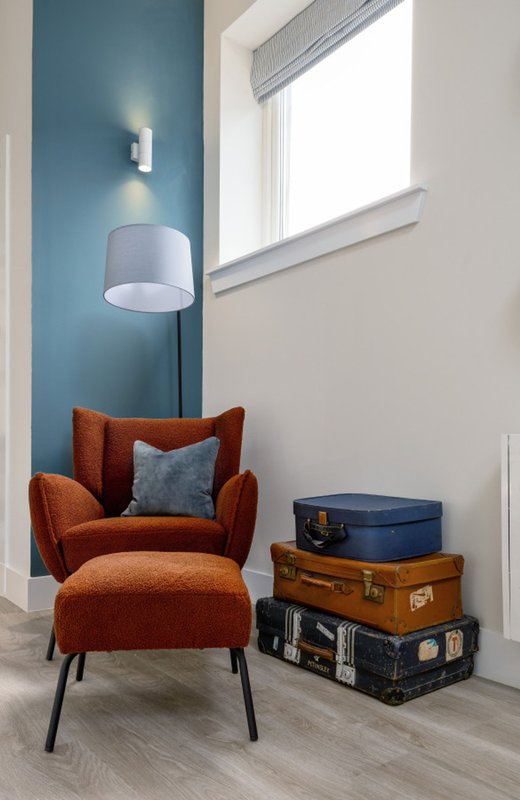 Modern corner seating area with burnt-orange armchair, pendant lamp, stacked vintage suitcases and bright window