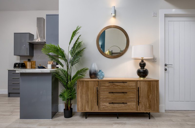 Modern living room with gray desk, wooden sideboard, round mirror, potted plant and lamp
