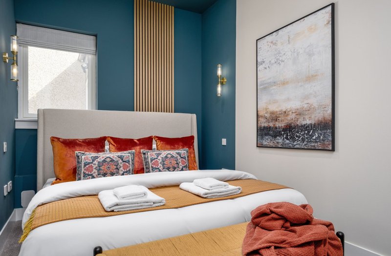Modern bedroom with blue accent wall, white bedframe, orange bedding and decorative pillows
