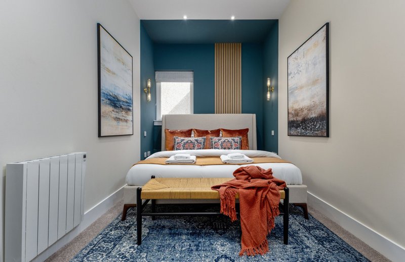 Modern bedroom with double bed, teal accent wall, orange bedding, and framed artwork