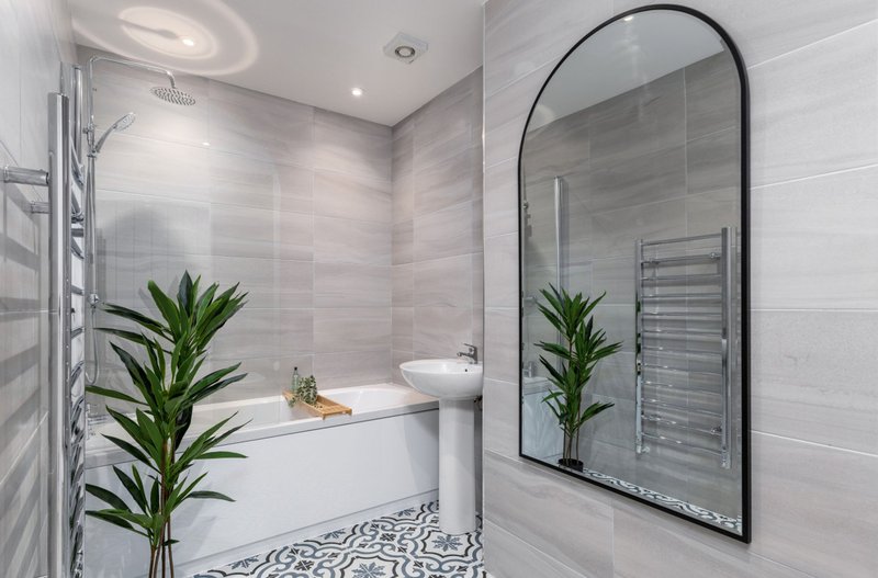 Modern bathroom with arched mirror, white sink, grey tile walls and potted plants