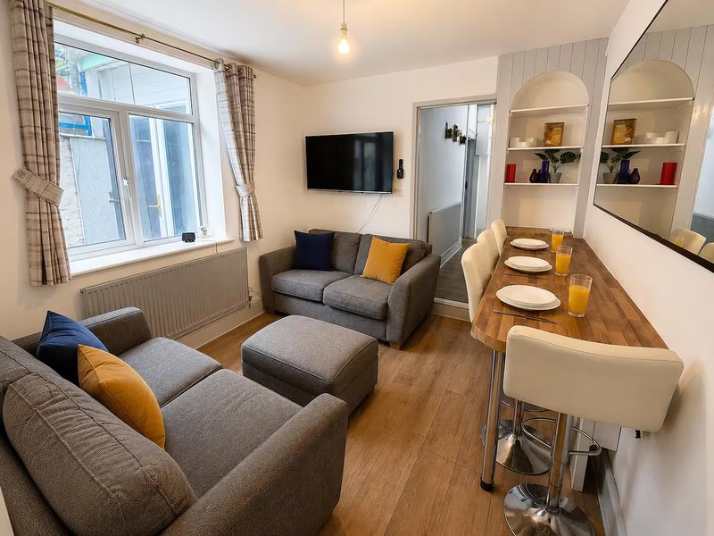 Open-plan living room with gray sofas, dining table, wall-mounted TV, and built-in shelving