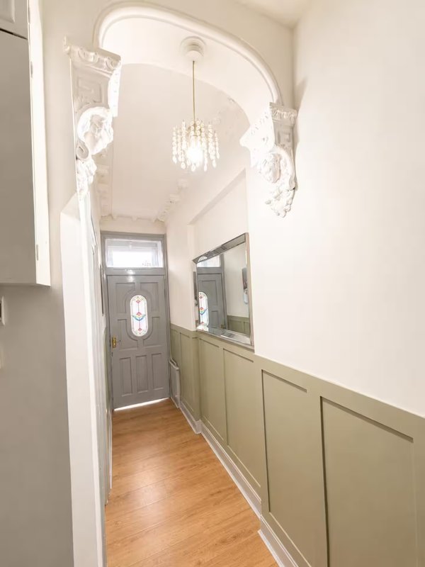 Hallway with arched doorway, pendant light, sage green panelling and wooden flooring