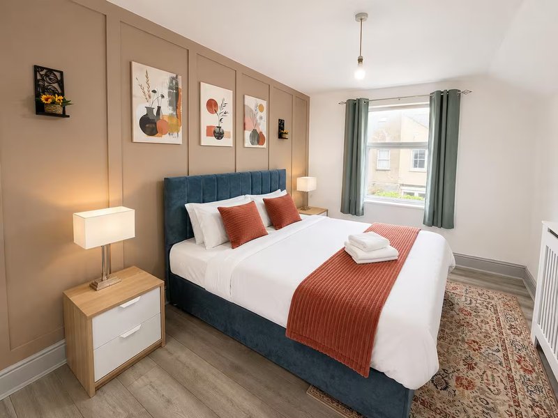 Modern bedroom with double bed, teal headboard, white bedding, rust-coloured throw and decorative pillows