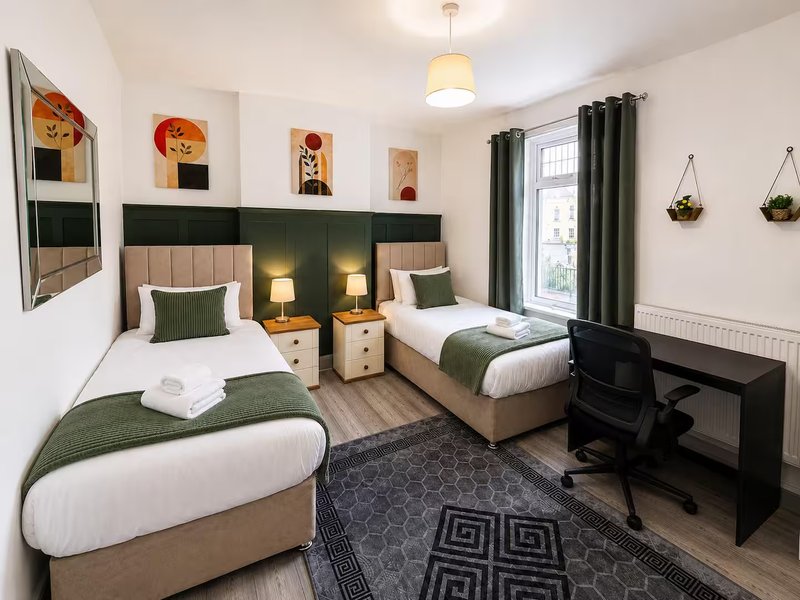 Twin bedroom with green headboards, white bedding, desk, and window with dark curtains
