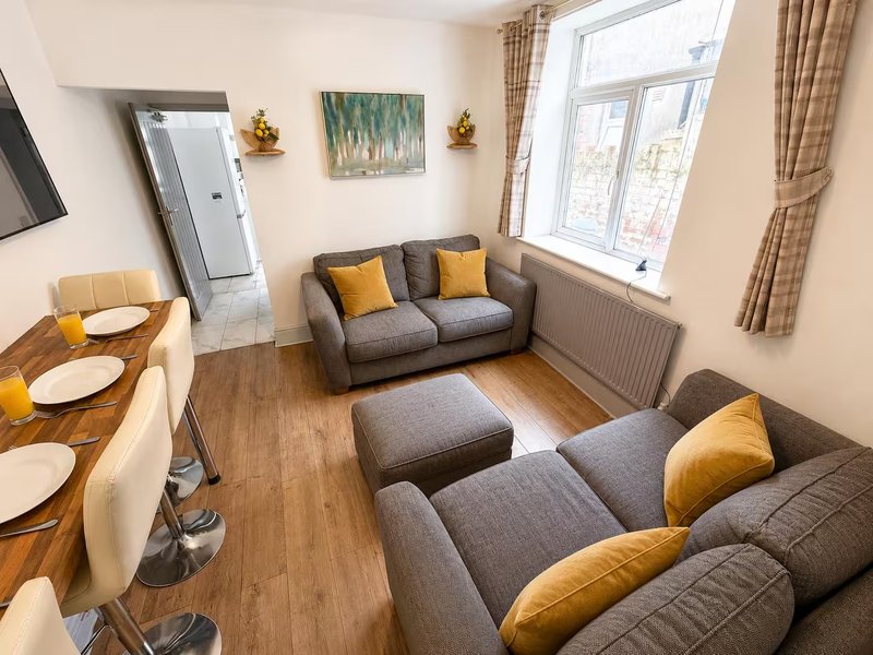 Open-plan living room with grey sofas, yellow cushions, dining table and large window