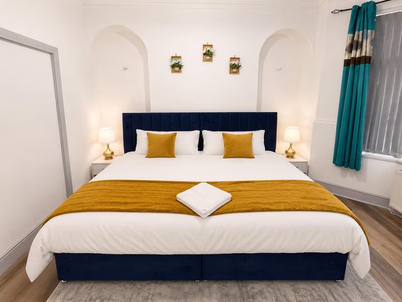 Modern bedroom with navy bed frame, white bedding, gold accents and wall sconces