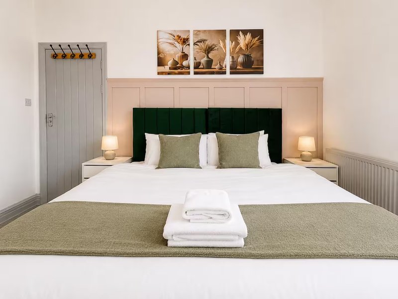 Modern bedroom with double bed, green headboard, white pillows, and framed wall art above