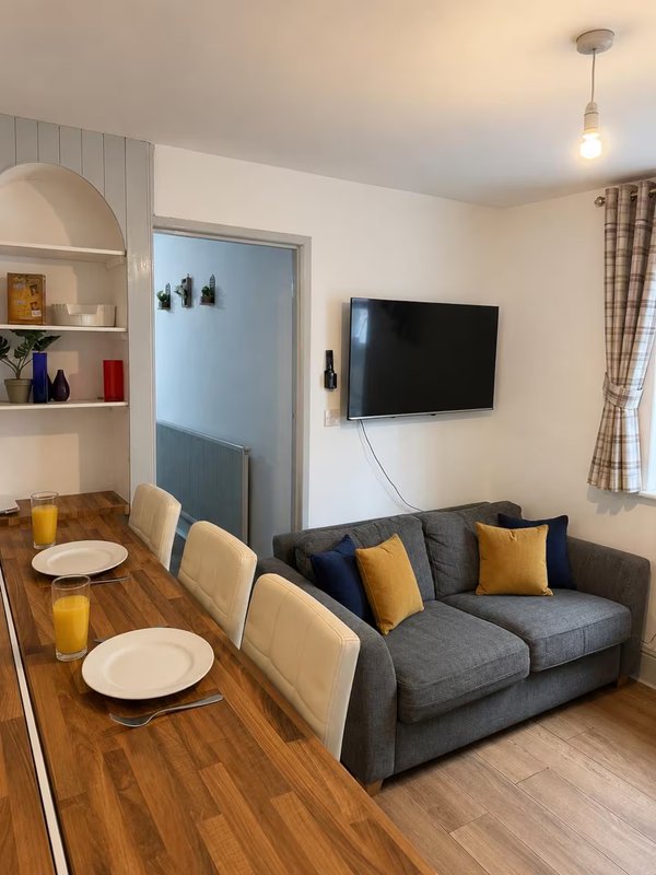 Open-plan living and dining area with sofa, wall-mounted TV, dining table and kitchen area