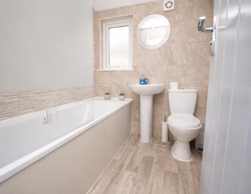 Bathroom with bathtub, pedestal sink, toilet, round mirror and small window